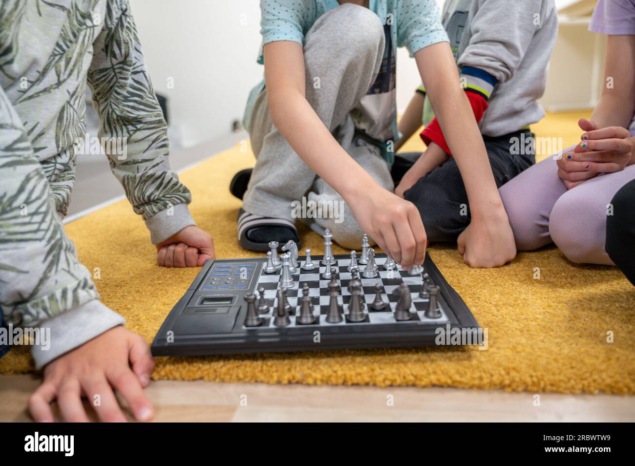 Children plays chess together with electronic board sitting on floor. No faces, unrecognizable persons Stock Photo