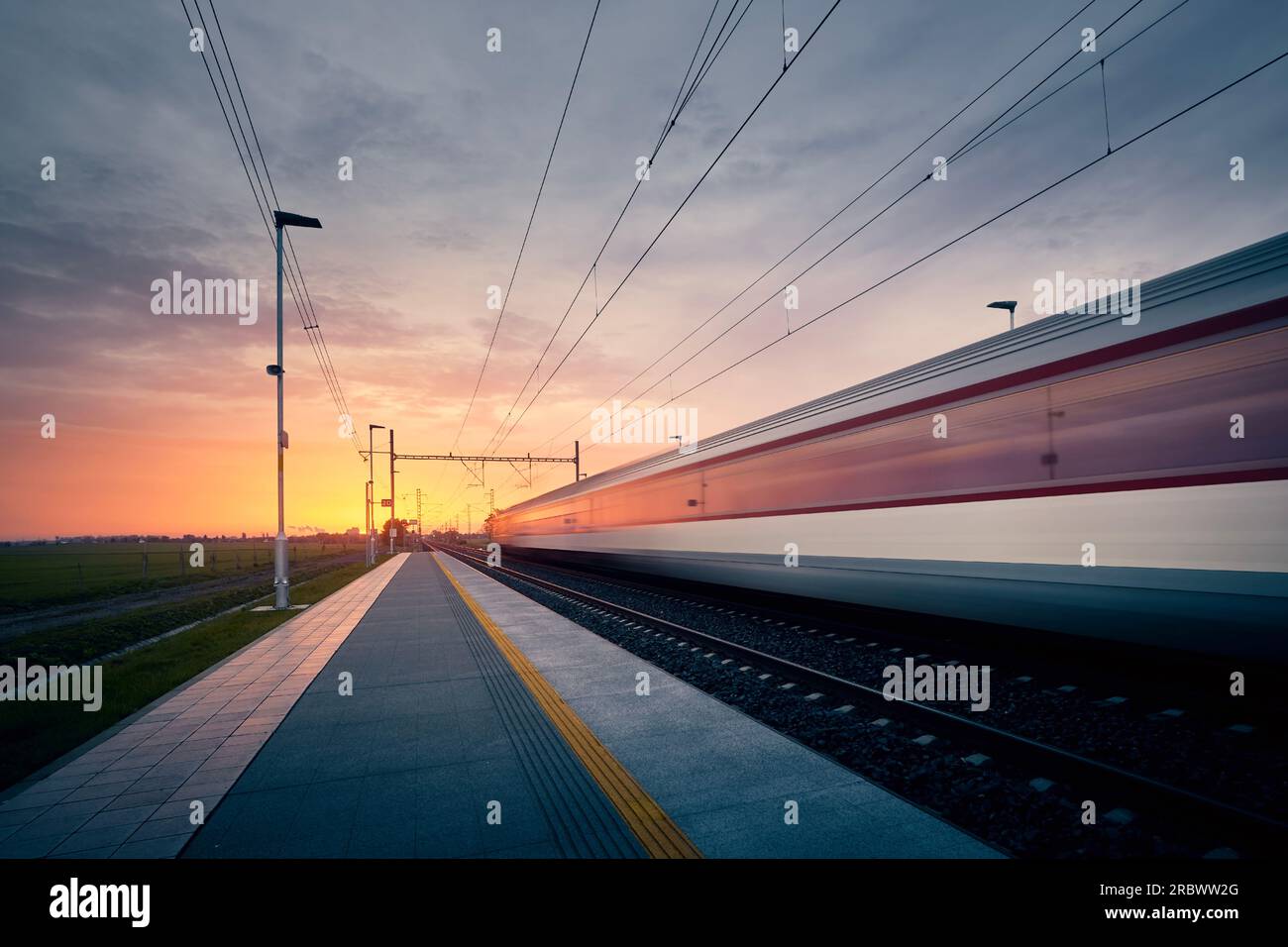 Railway at beautiful dawn. Long exposure of train on railroad track. Moving modern intercity passenger train. Stock Photo