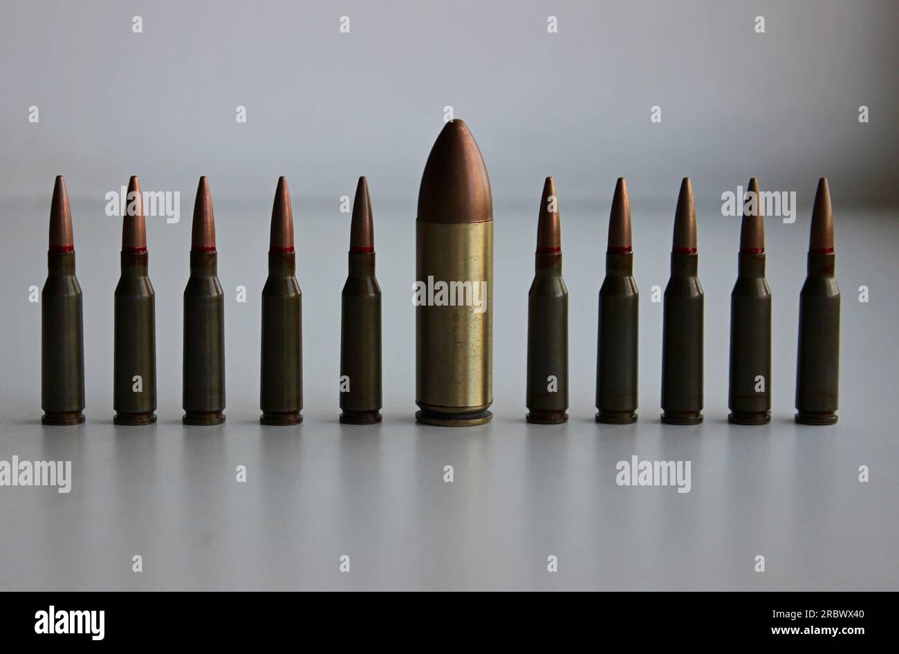 A line of identical regular caliber bullets with one huge large caliber bullet front view detailed stock photo Stock Photo