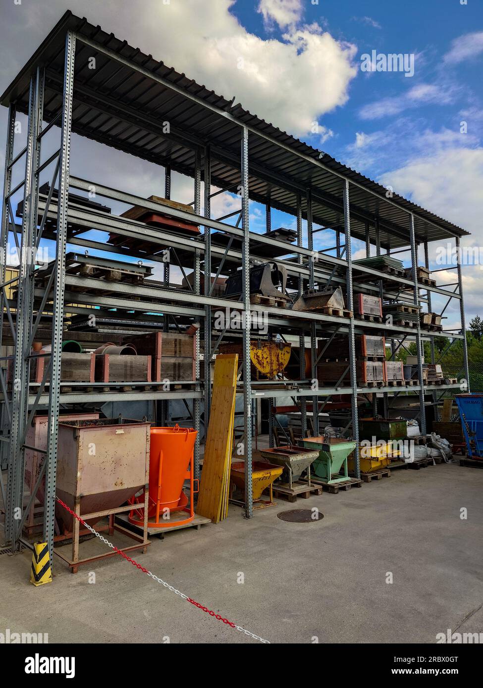 Construction site stacked storage shelves with pallets, cement mixers and raw materials. Exterior shot, sunny blue sky, no people. Stock Photo
