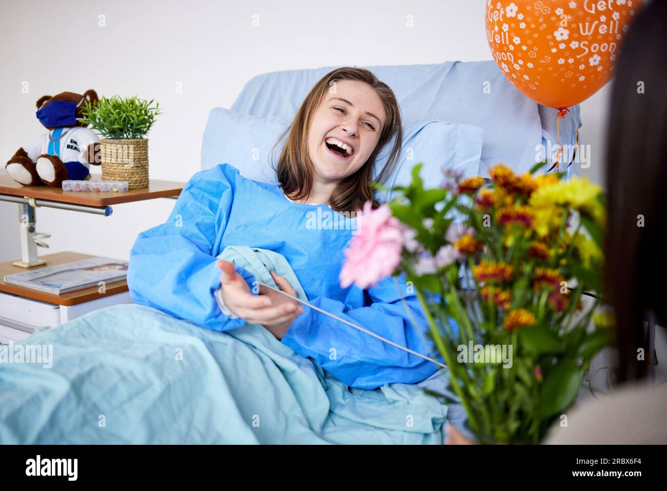 Sick, hospital patient and visitor with flowers at bed with a woman in
