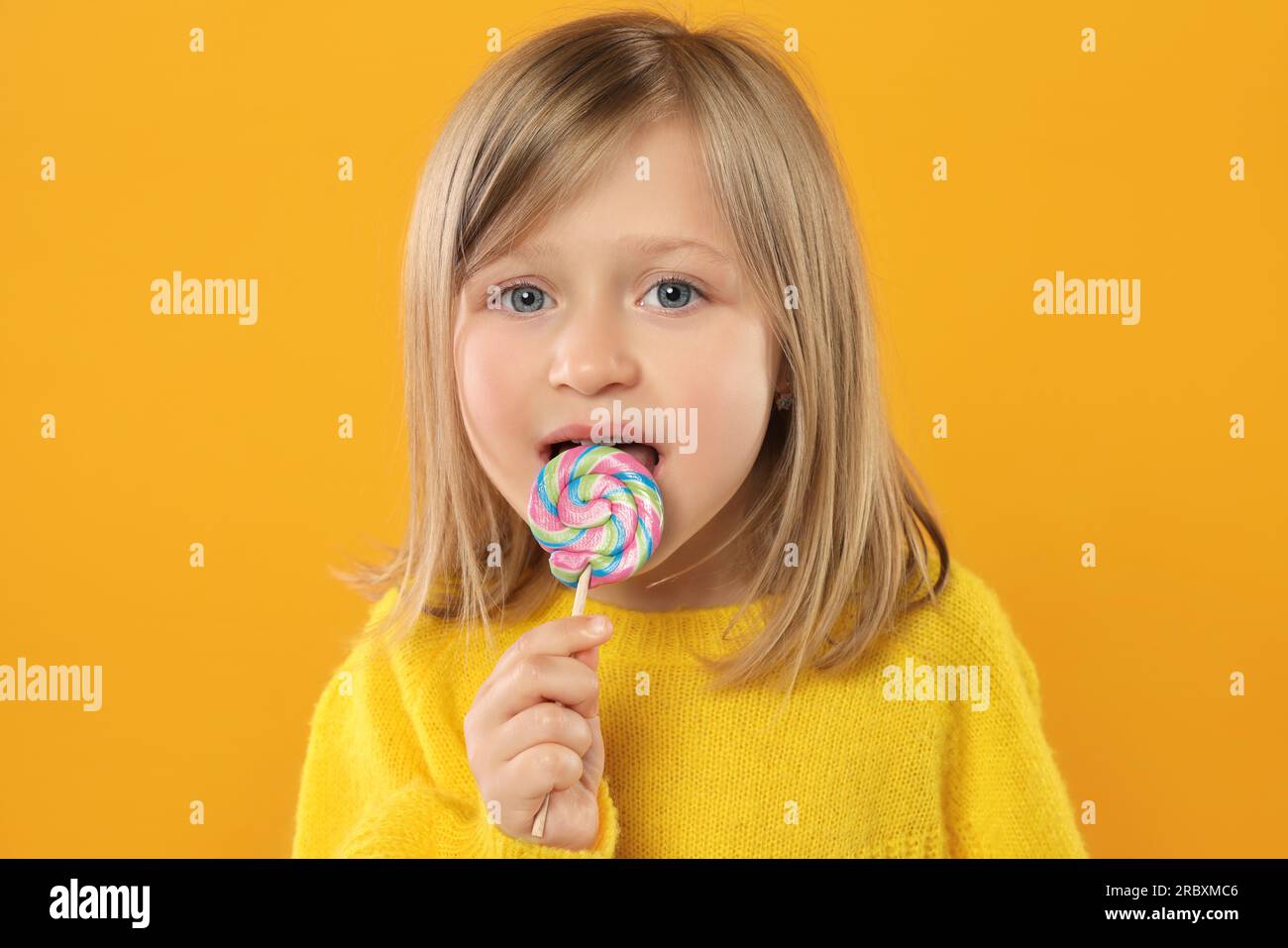 Portrait Of Happy Girl Licking Lollipop On Orange Background Stock