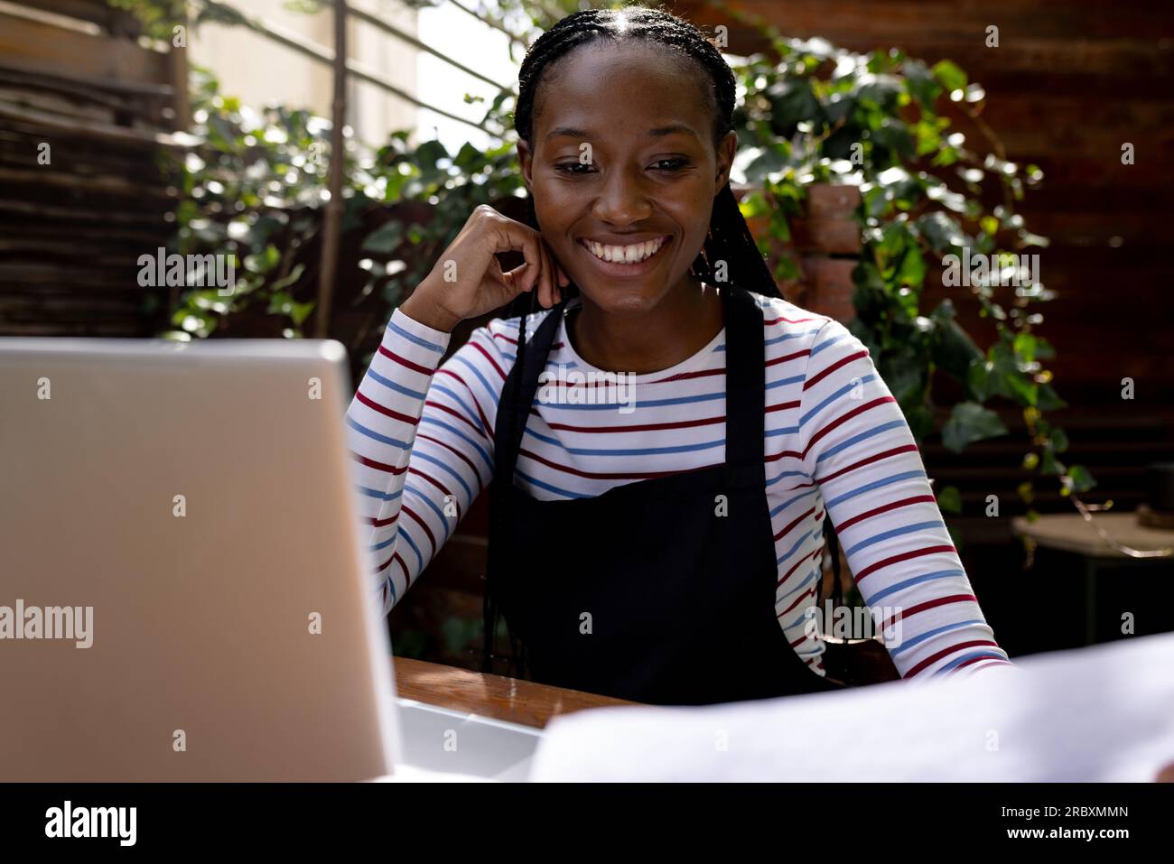 Happy african american female coffee shop owner in apron using laptop