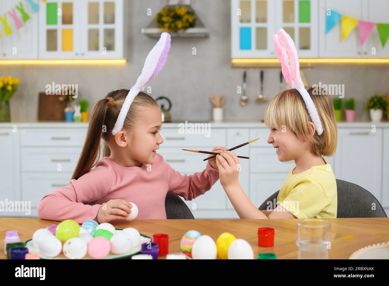 Children having fun while painting Easter eggs at table in kitchen Stock Photo