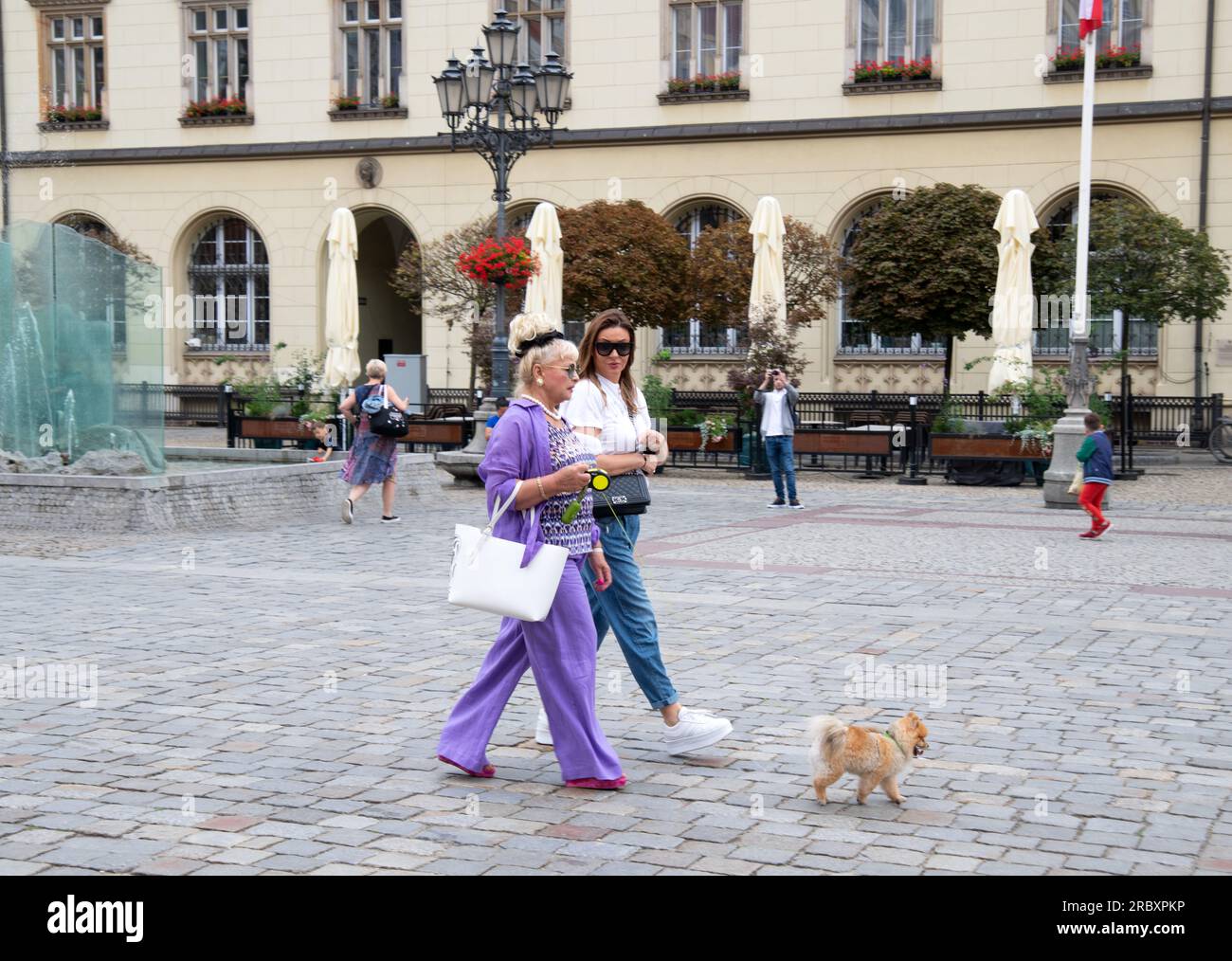 Two ladies taking dog for walk, in Rynek Square, Wroclaw, Poland Stock Photo