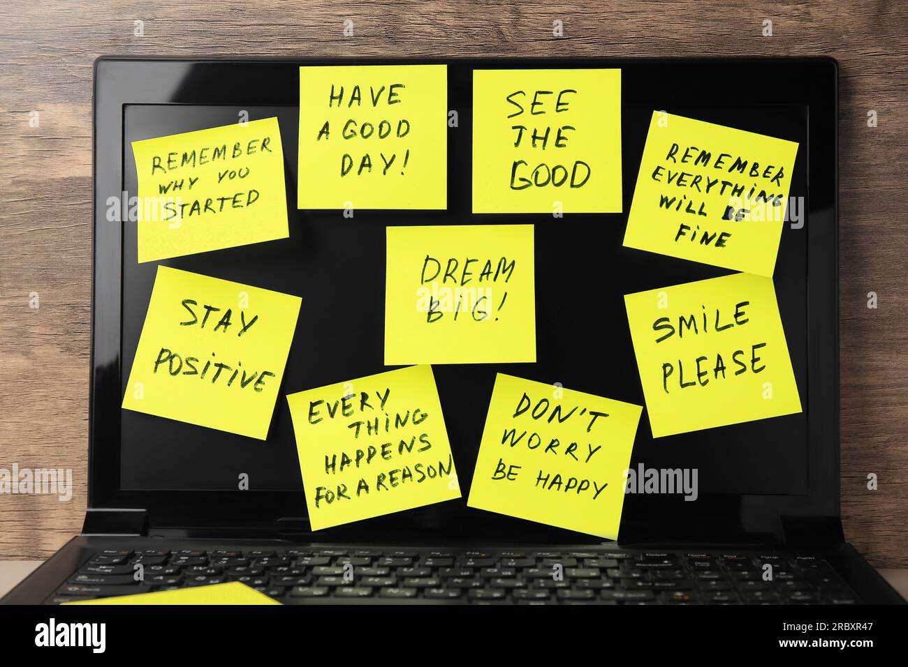 Paper notes of life-affirming phrases on laptop against wooden background Stock Photo
