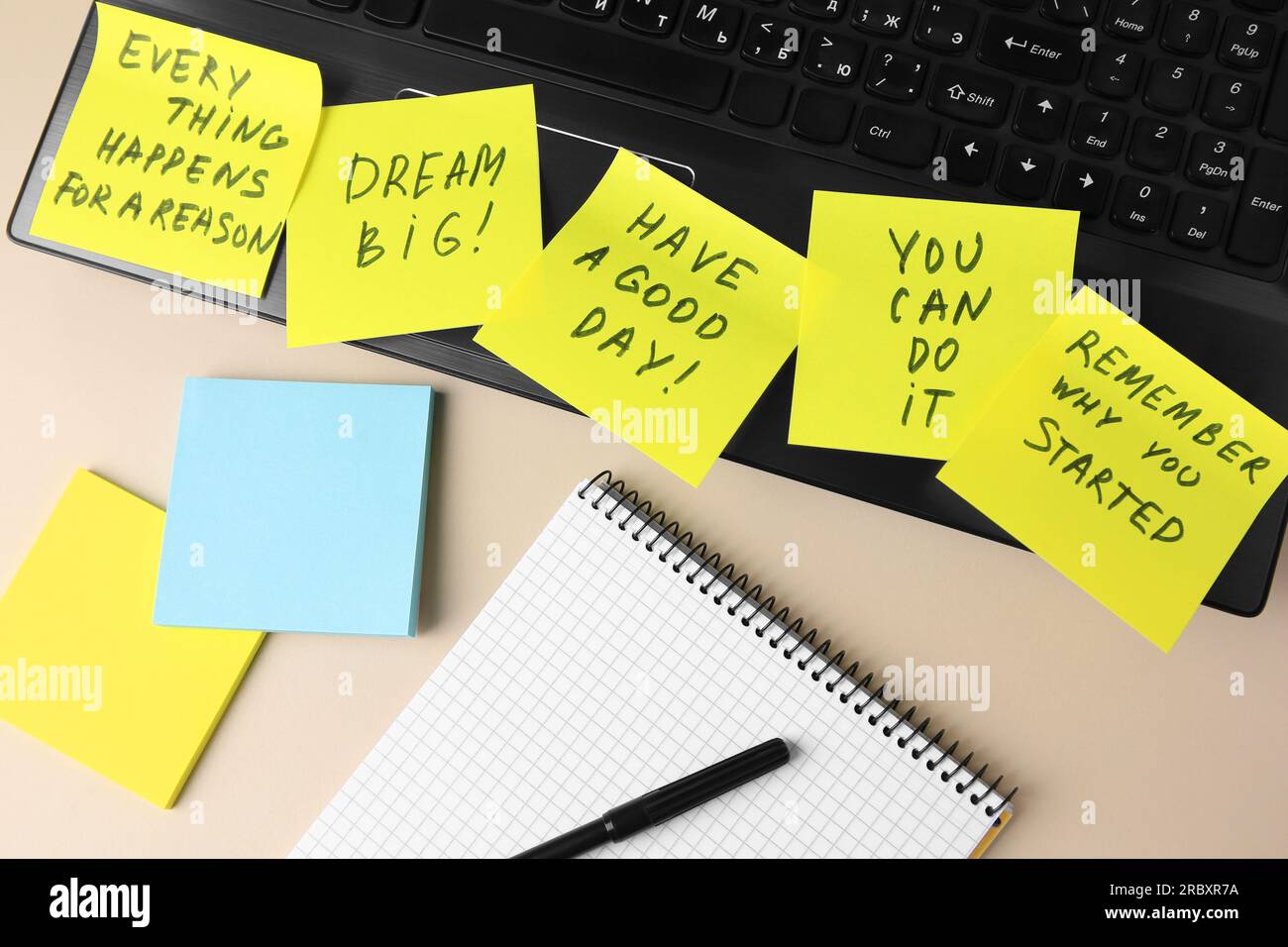 Laptop with paper notes of life-affirming phrases and notebook on beige desk, flat lay Stock Photo