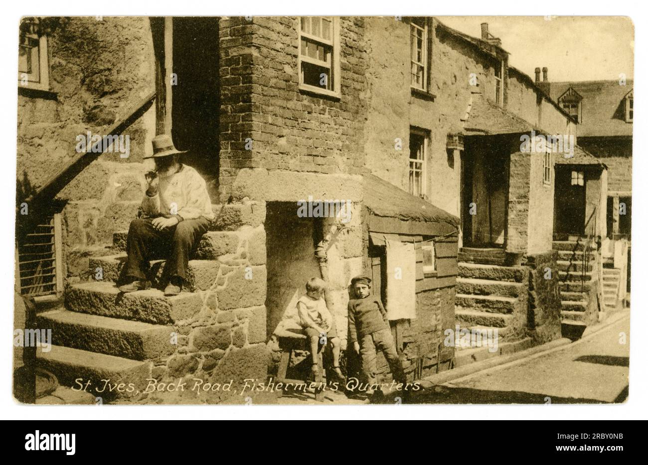 Original early 1900's postcard of fisherman smoking a pipe on steps to a traditional Cornish stone cottage in the fishermen's Quarters, Back Road East, St. Ives. The characters are Mr. Ninnis, Sammy Phillips and Jack Richards. Stock Photo