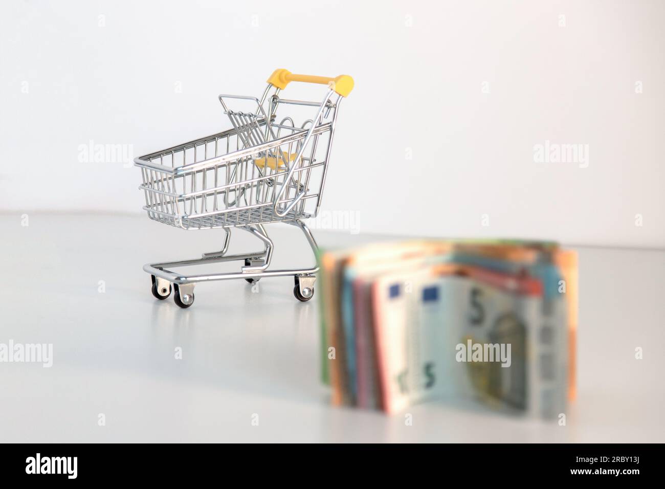 Supermarket shopping cart with essential goods and several euro banknotes on a white background. Conceptual image about purchasing power. Stock Photo