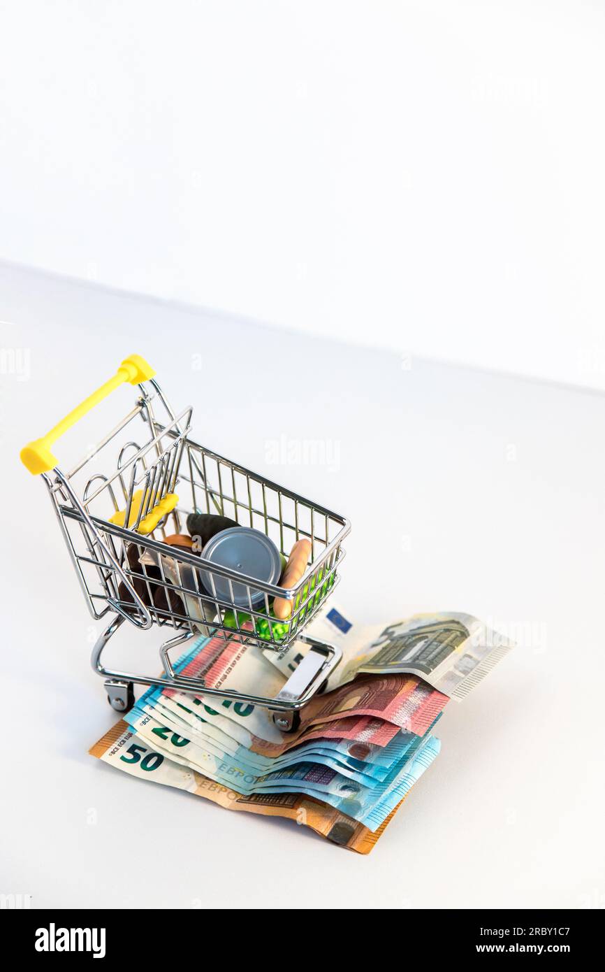 Supermarket shopping cart with essential goods and several euro banknotes on a white background. Conceptual image about purchasing power. Stock Photo