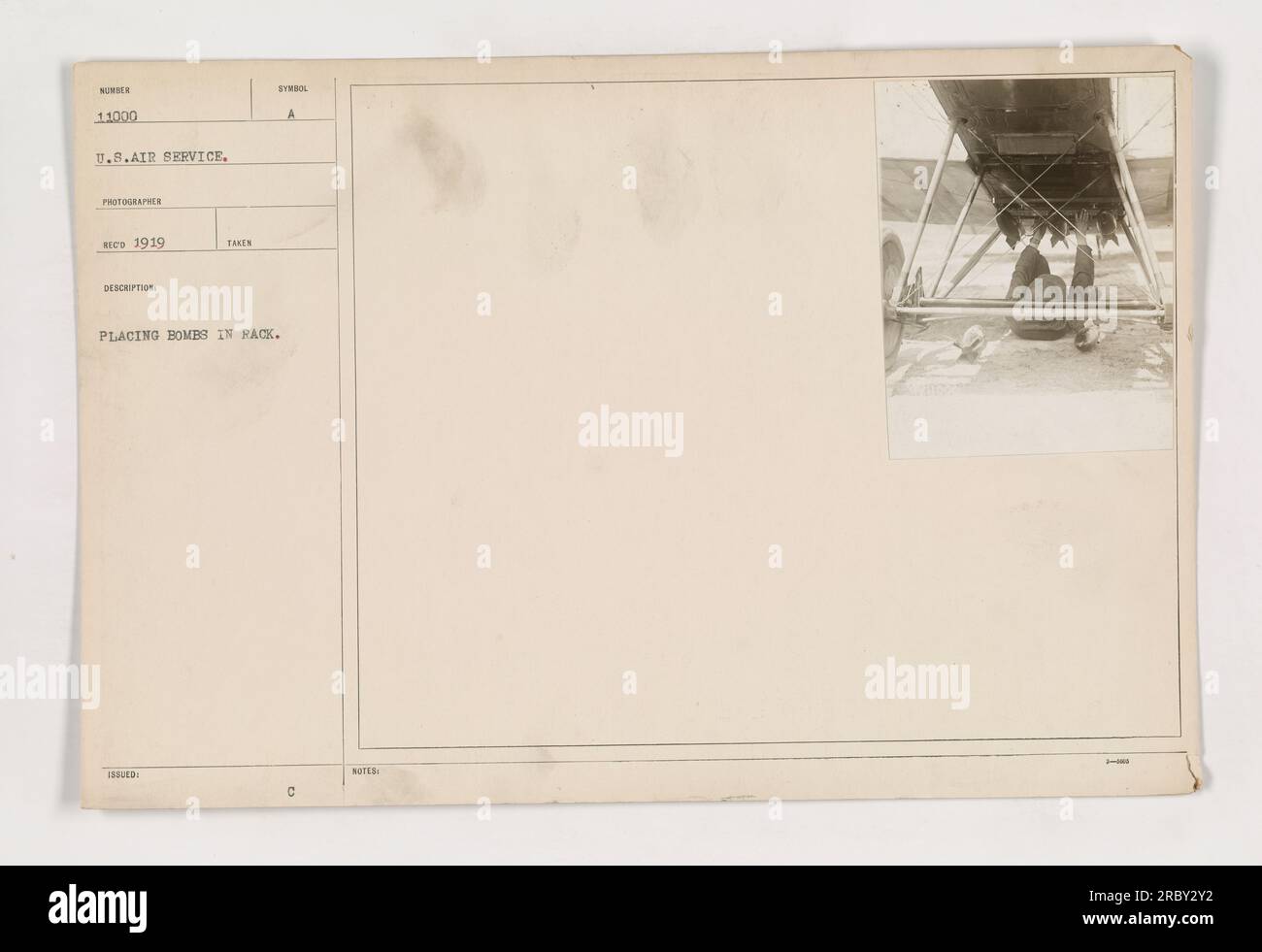 A U.S. Air Service photograph taken in 1919 shows a soldier placing bombs in a rack. This image captures a training exercise during World War I, demonstrating the process of loading explosives onto an aircraft. The careful precision evident in the soldier's actions illustrates the importance of proper bomb placement in military operations. Stock Photo