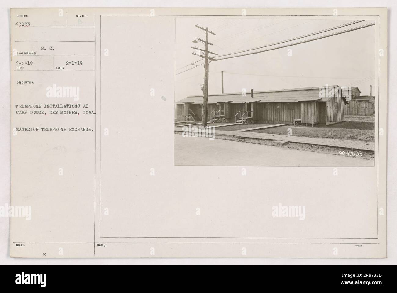 This photograph depicts an exterior view of a telephone exchange at Camp Dodge, Des Moines, Iowa. The image was taken on February 1, 1919, as documented by the assigned photographer. The photo is part of a larger collection capturing various military activities during World War One. Stock Photo