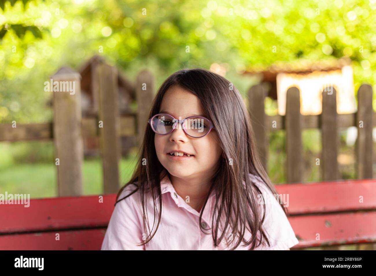 Portrait of a cute little girl wearing glasses sitting on a bench Stock ...