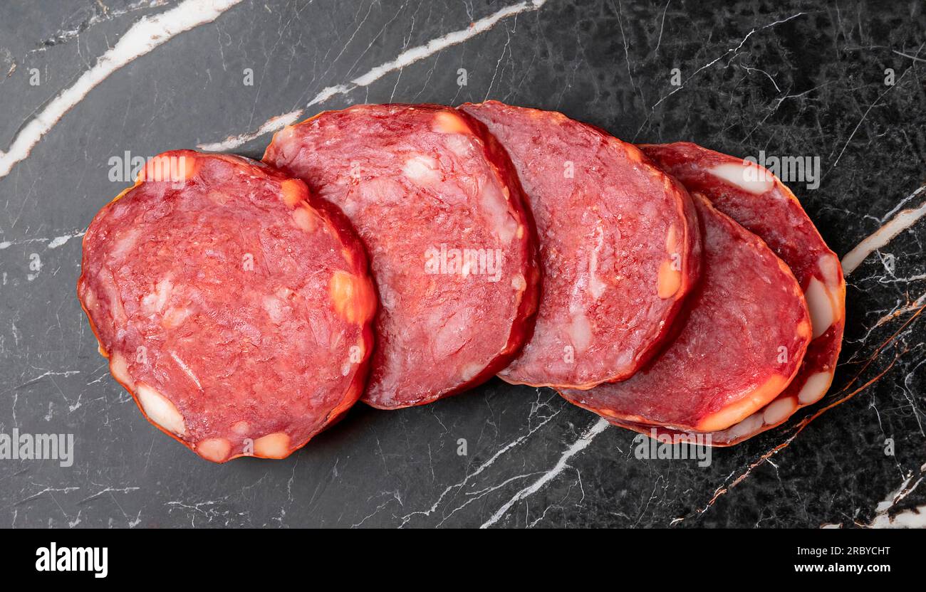 macro photo of raw dried sliced horse meat sausage on black marble surface top view Stock Photo