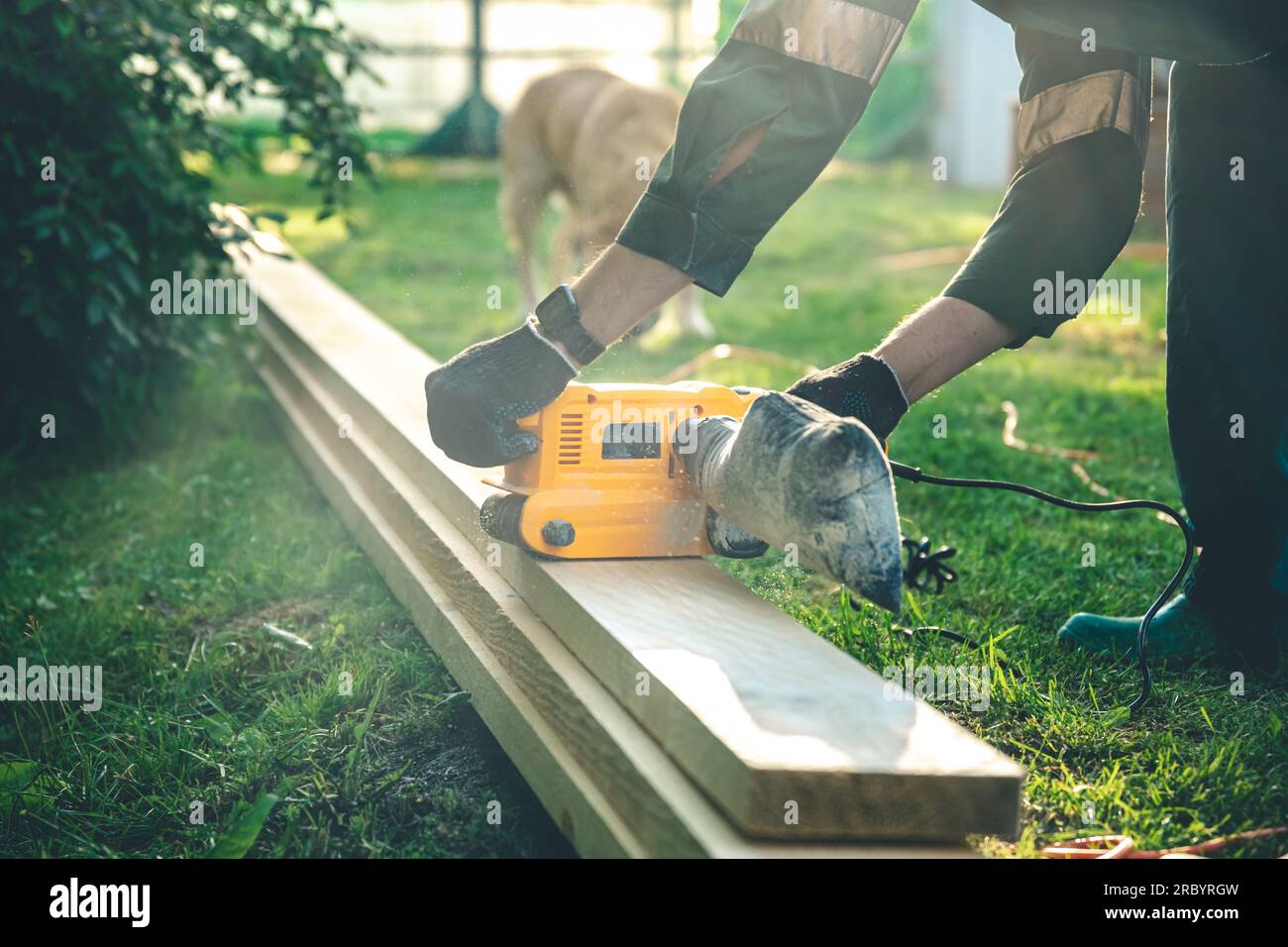 The man grinds the boards with a belt grinder, the electric tool for
