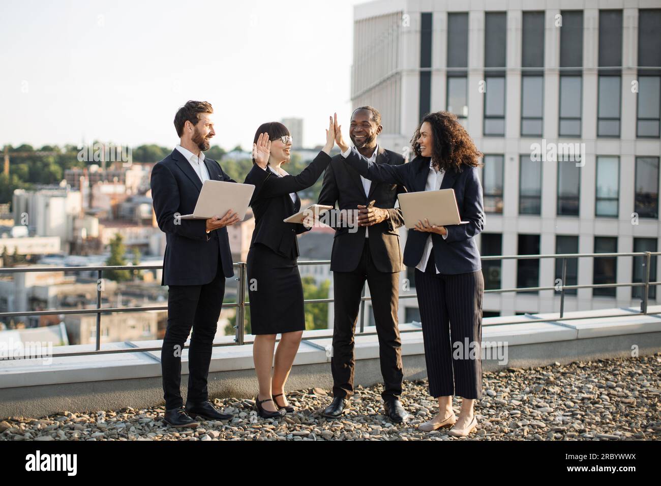 Male and female developers celebrating achievement of business goal and giving high five to each other. Successful colleagues meeting at office roofto Stock Photo