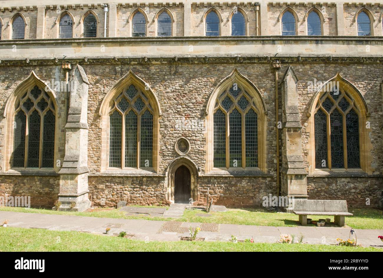 Part of Llandaff Cathedral facing south showing two layers of windows, a small 'side door' and a bench - all enjoying the sun. Stock Photo