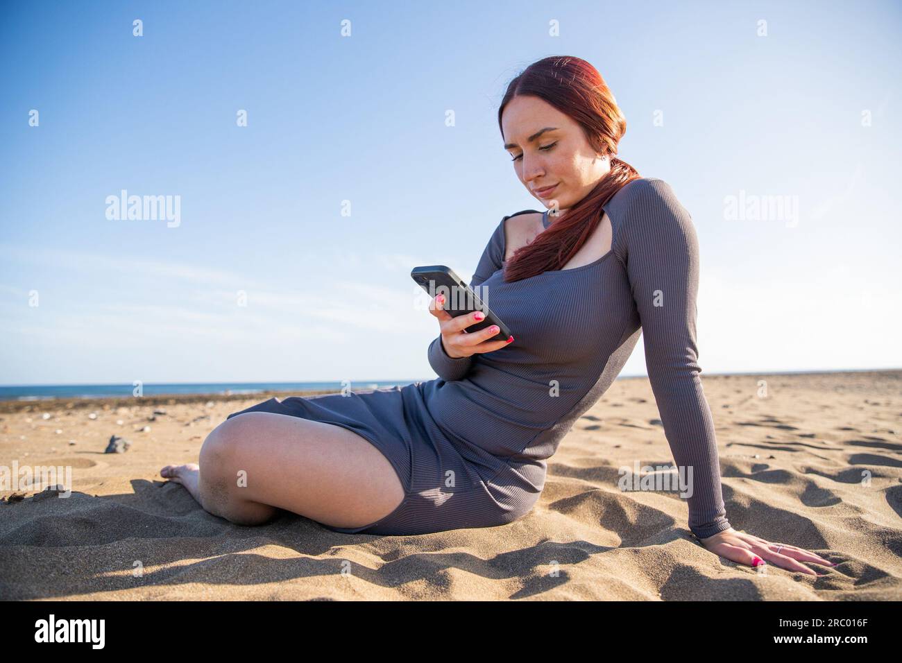 A girl uses her smartphone sitting at the beach in summer, technology on vacation Stock Photo