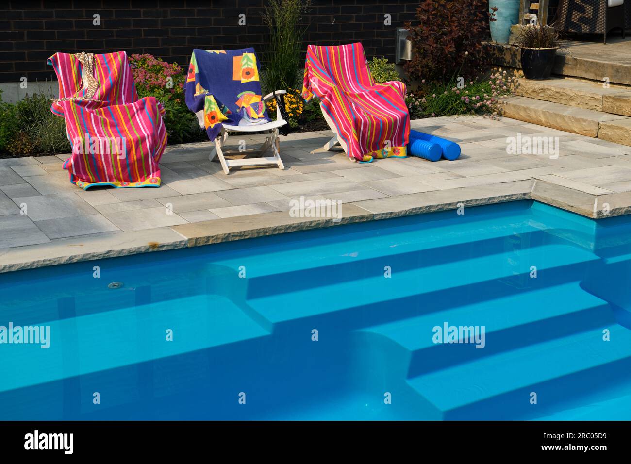 Deck chairs with drying beach towels on patio deck next to home garden