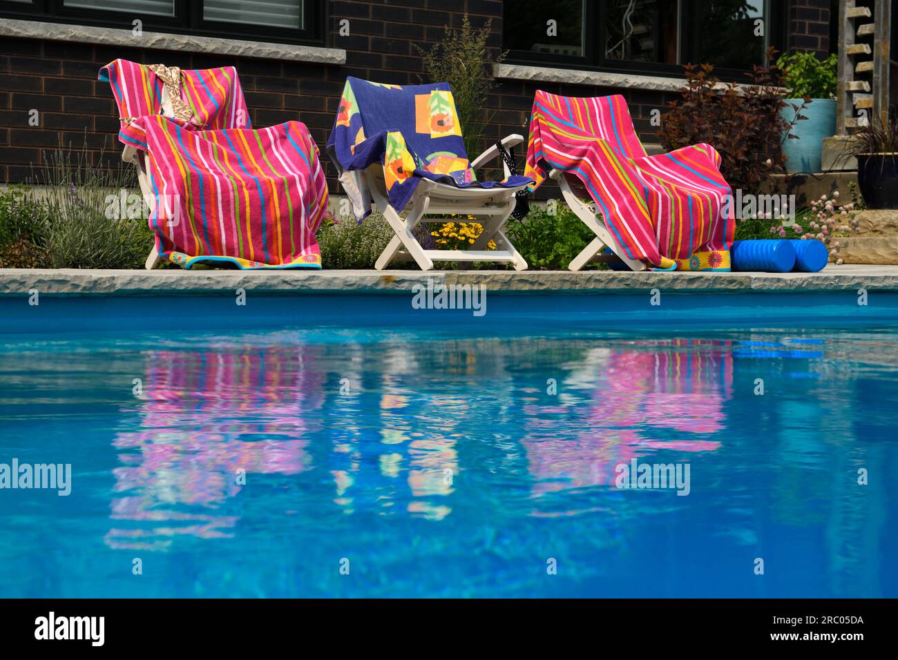 Pink beach towels reflected in rippling blue swimming pool water in backyard with garden Stock Photo