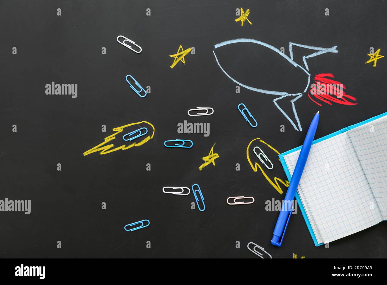 Creative composition with drawn rocket and different stationery on black chalkboard Stock Photo