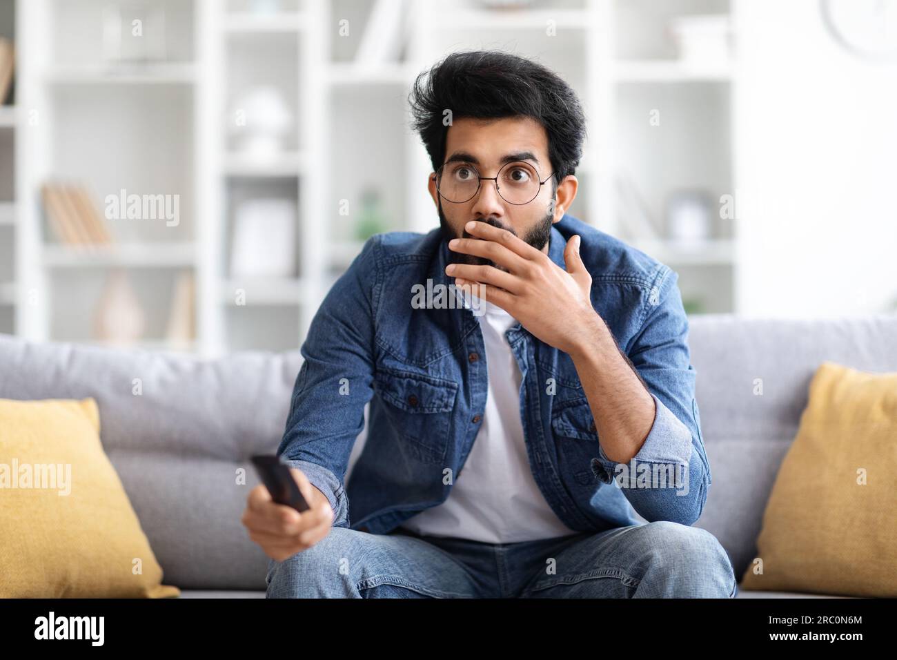 Shocked Indian Man With Remote Controller In Hand Sitting On Couch Stock Photo