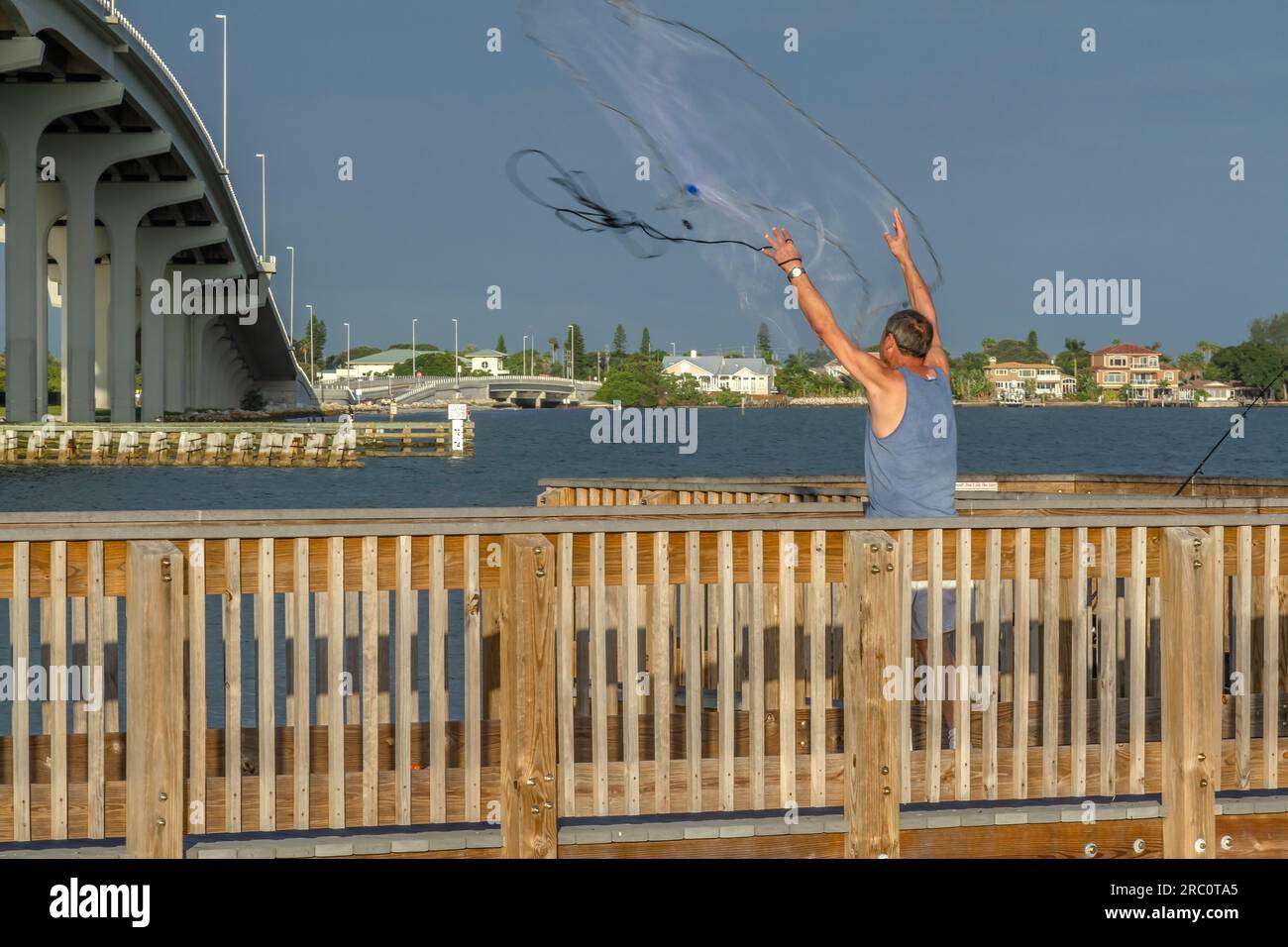 Single adult male cast net fishing off a river pier in the Tampa, Florida area. Man has just released the net. Stock Photo