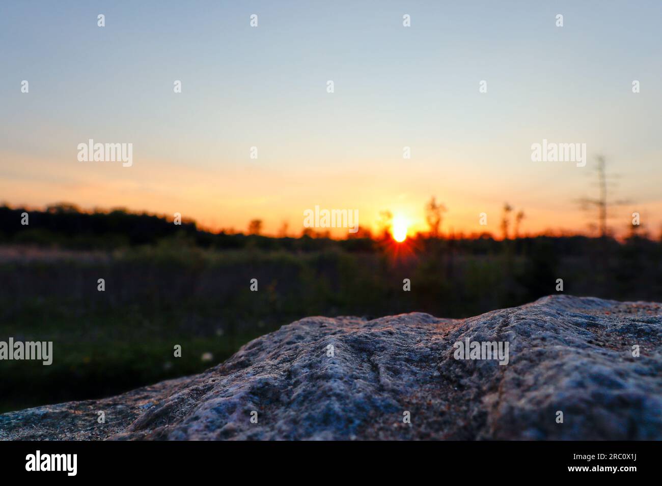 Sunset landscape - grass field - rock in foreground. Taken in Toronto, Canada. Stock Photo