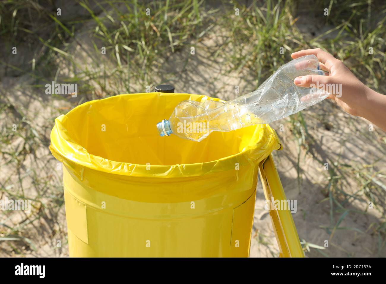 Woman throwing plastic bottle in yellow bin on beach, closeup