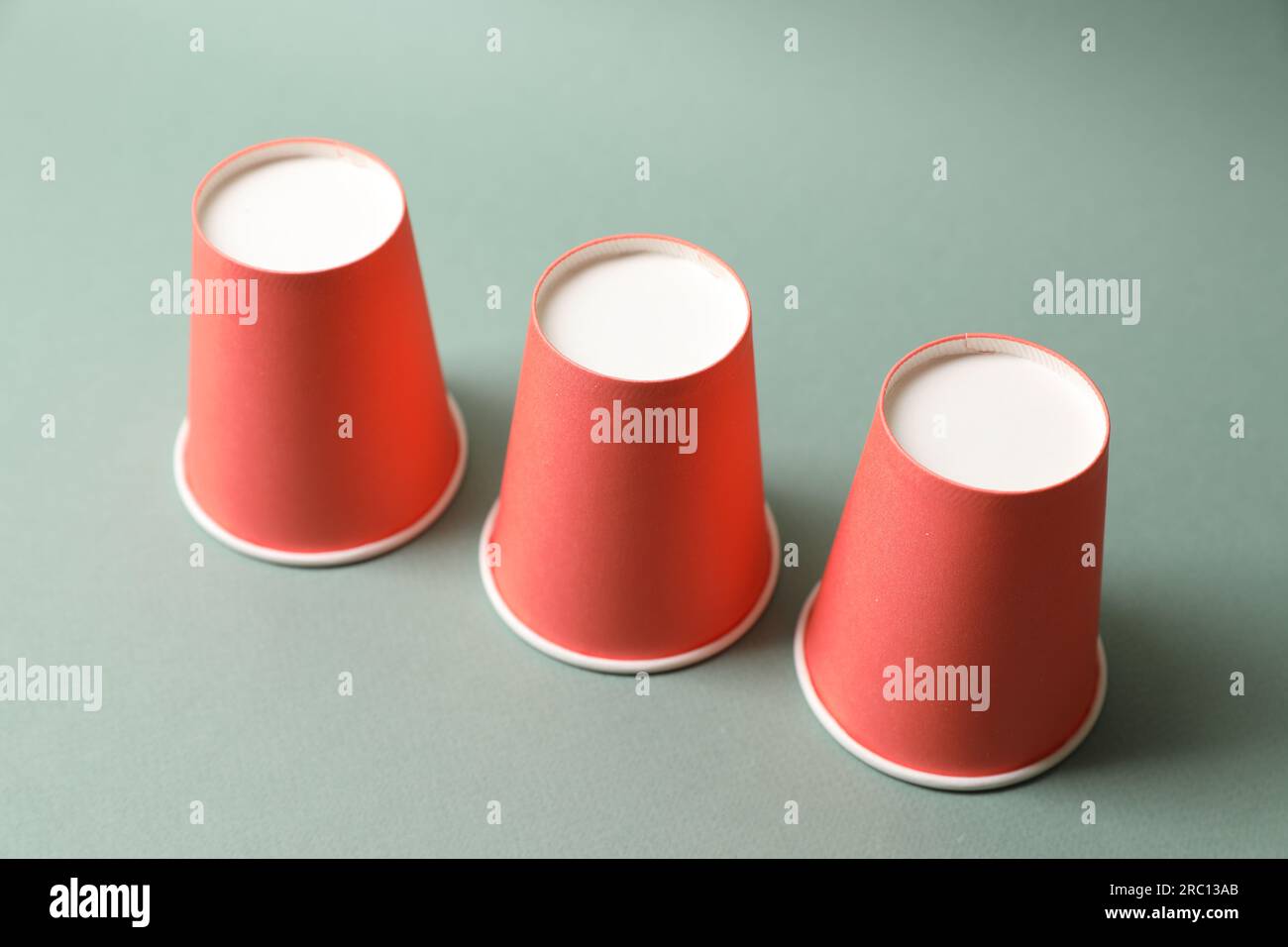 Three red cups on pale olive background. Thimblerig game Stock Photo ...