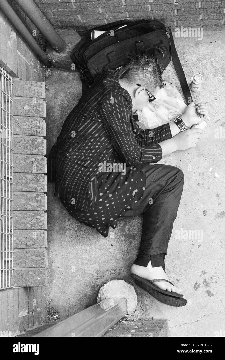 A homeless young man passed out on a sidewalk, surrounded by empty cans of lighter fluid, at Darlinghurst in East Sydney, Australia. The inhaling of lighter fluid fumes creates a low-cost 'high' that is favoured by some users of illicit drugs. Stock Photo