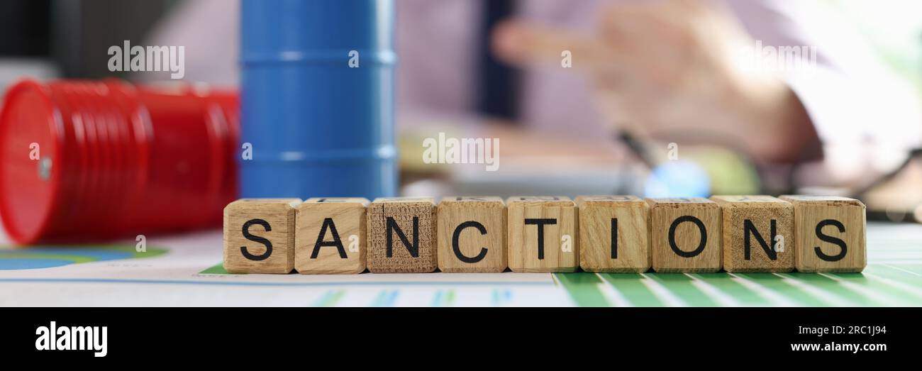 Oil drums on financial statements, word sanction and business man in background. Stock Photo