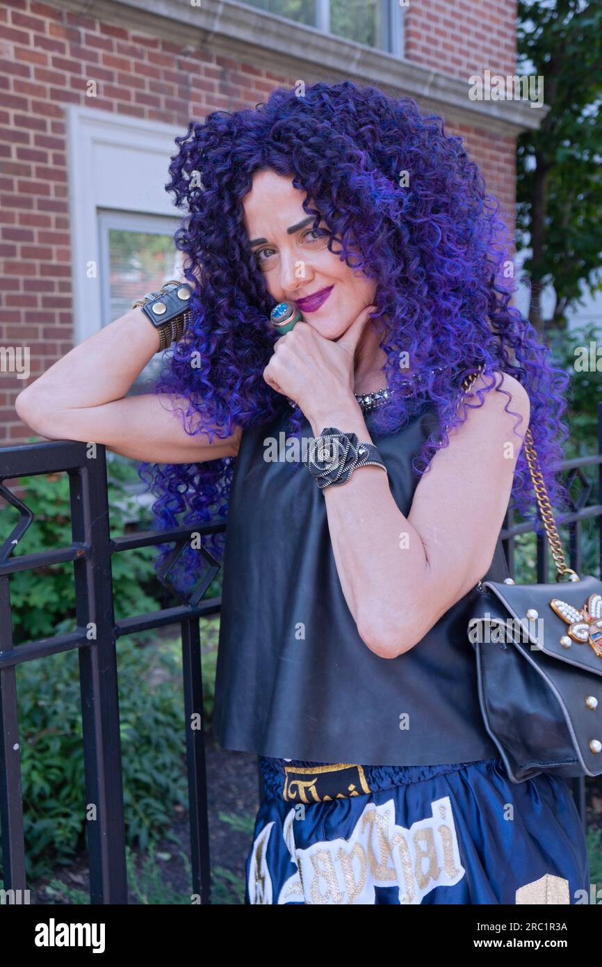 A fifty year old woman looking youthful with long purple curly hair and a summer outfit in Greenwich Village, New York City Stock Photo