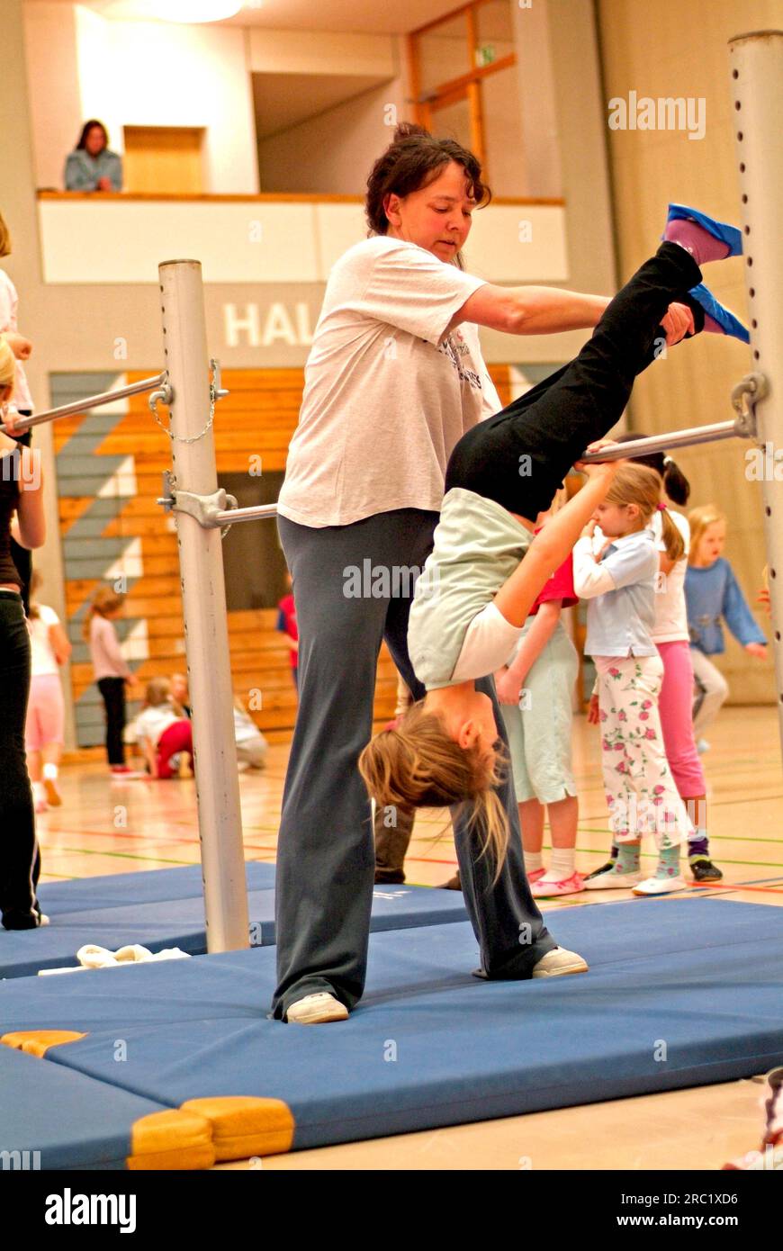 Sports teacher holding girl at high bar, gymnasium, Oberstdorf, Bavaria