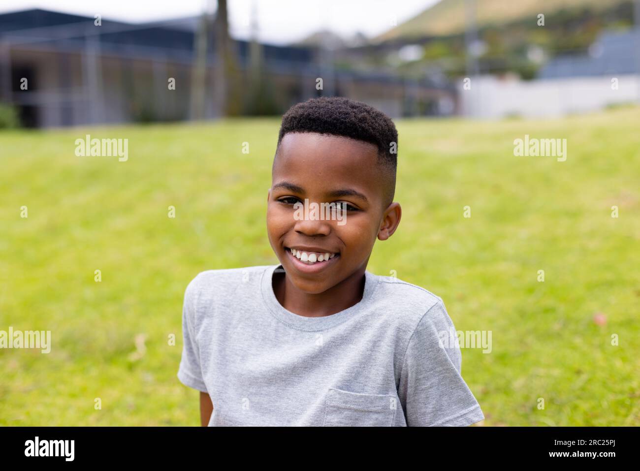 Portrait of happy african american schoolboy sitting on grass at school ...