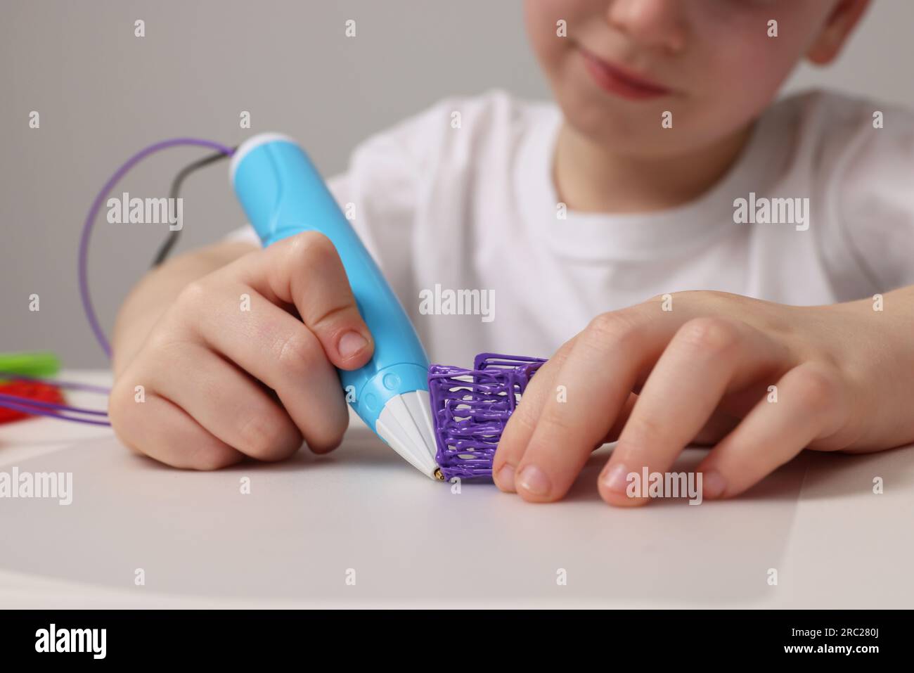 Boy drawing with stylish 3D pen at white table, closeup Stock Photo