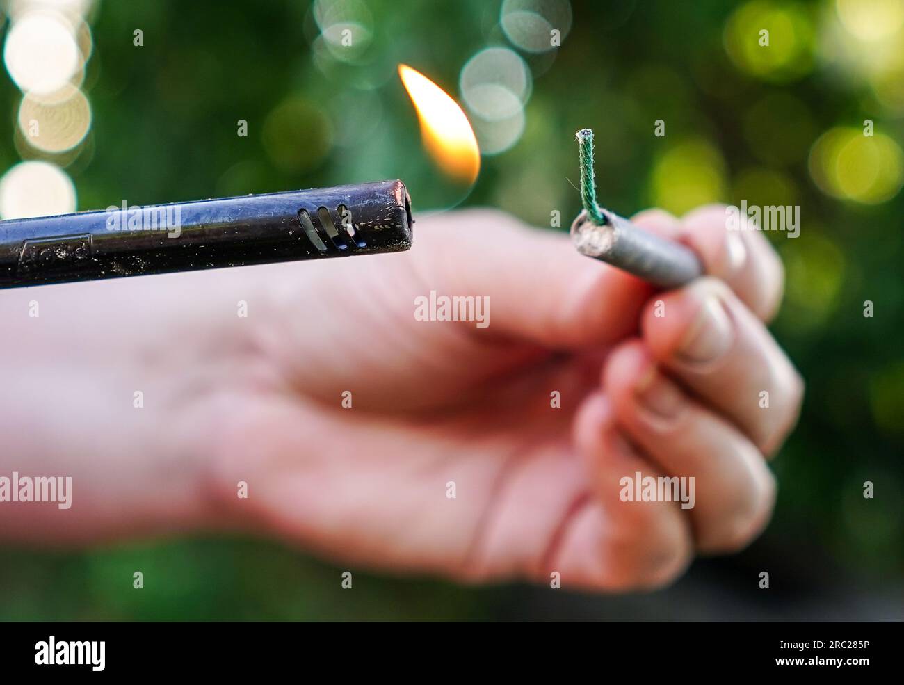 Person fire up firecracker. Person holding lighter and firecracker. Shooting firecrackers and fireworks. Stock Photo