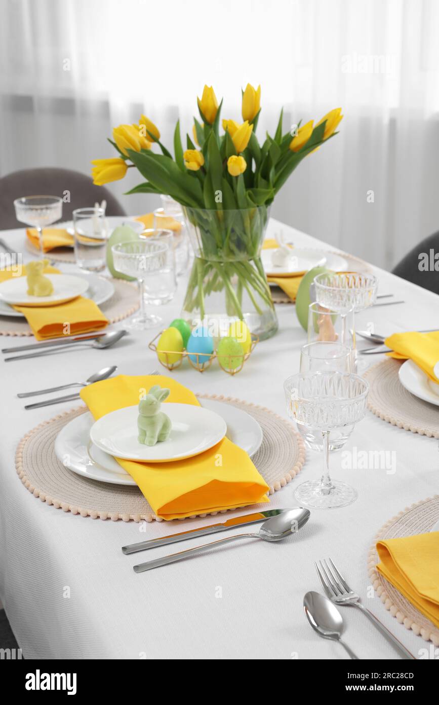 Festive table setting with glasses, painted eggs and vase of tulips ...