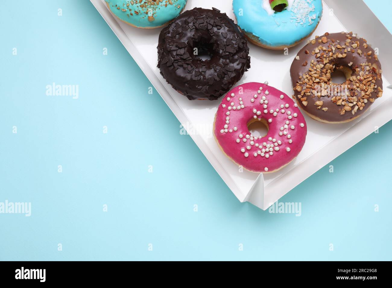 Box with different tasty glazed donuts on light blue background, top ...