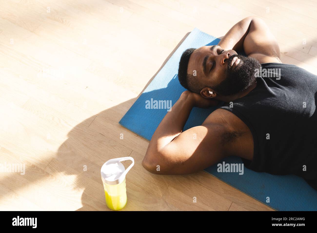 Relaxed african american man wearing sportswear with bottle of juice and  lying on mat at home Stock Photo - Alamy