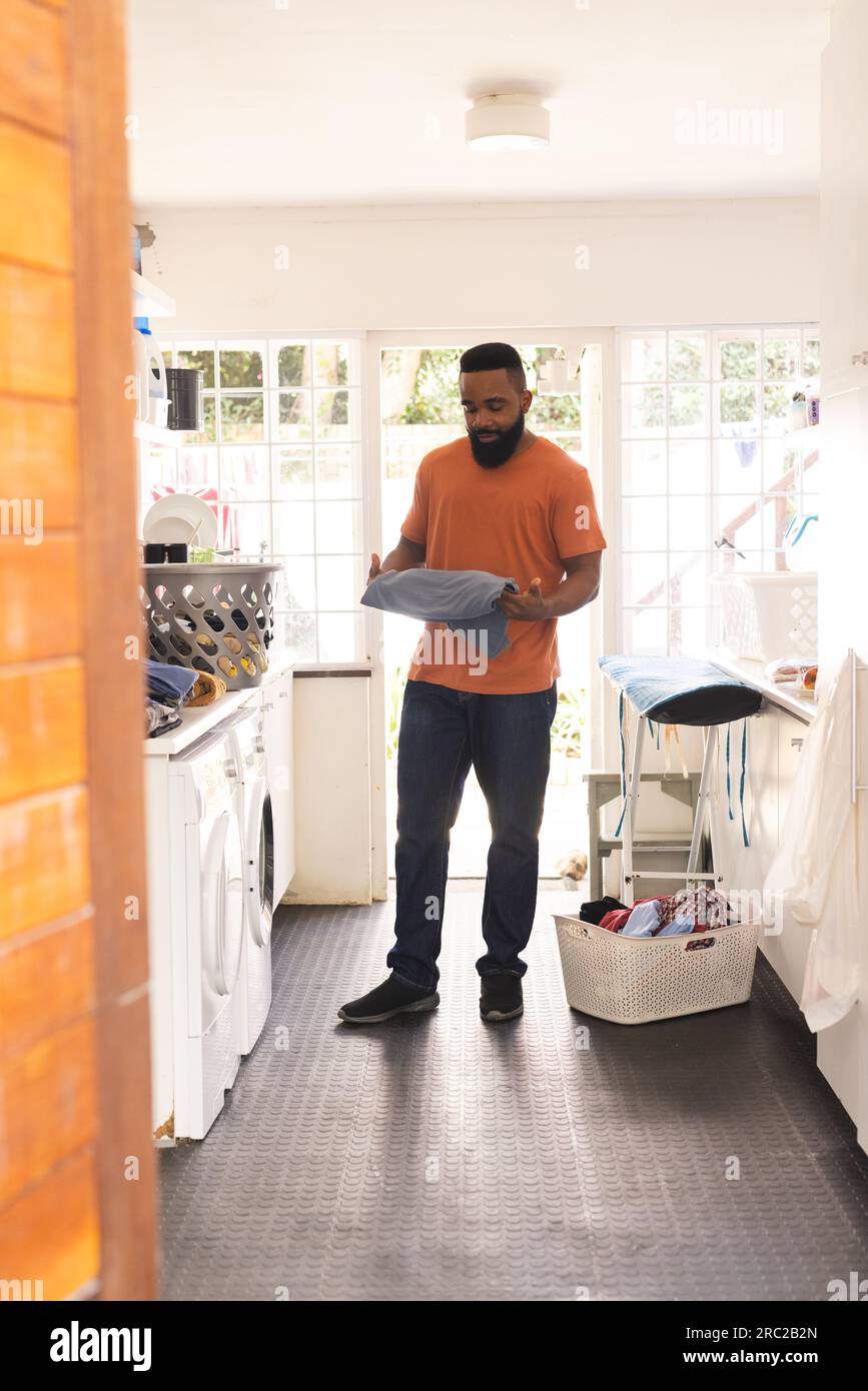 Happy african american man holding washing in kitchen with washing machine Stock Photo