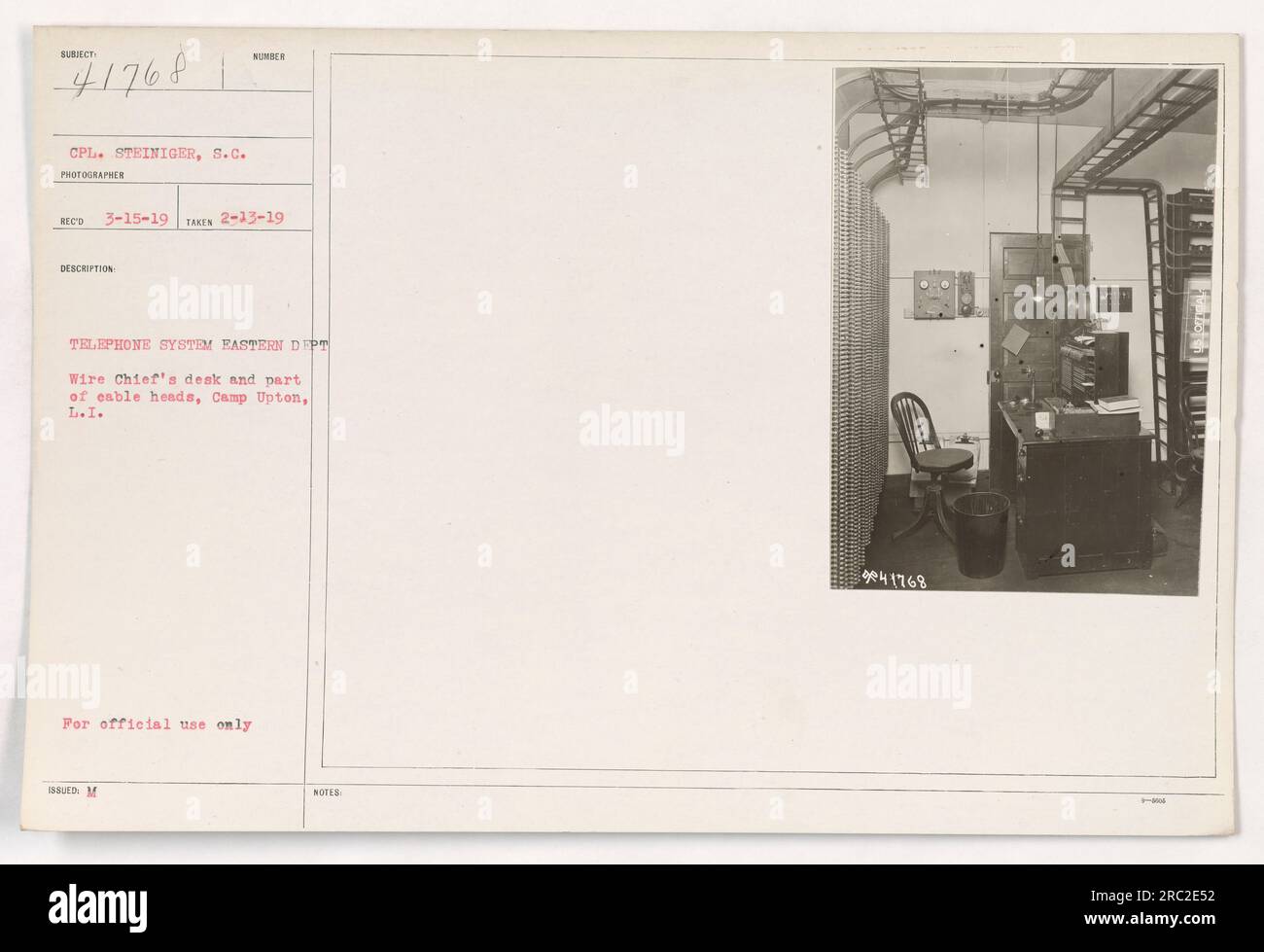 Camp Upton, Long Island. This image shows Corporal Steiniger, the S.C. photographer from the Eastern Department, at the Wire Chief's desk. The photograph was taken on February 13, 1919 and is part of description number 111-SC-41768. The image captures a section of the telephone system and cable heads. It is marked for official use only. Stock Photo