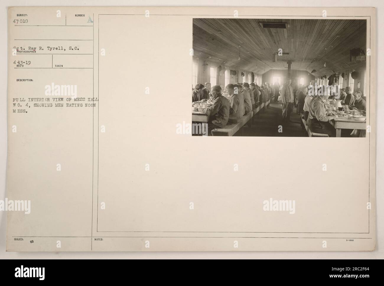 A photograph depicting a full interior view of Mess Hall No. 4 during World War I. Men can be seen eating their midday meal. The image was taken by Sergeant Ray R. Tyrell, S.C., and is labeled as Subject 47 010. The photograph is part of the collection numbered 443-19. Stock Photo