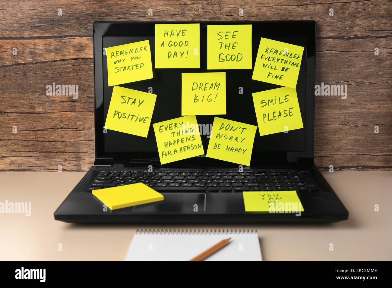 Laptop with paper notes of life-affirming phrases on beige desk indoors Stock Photo