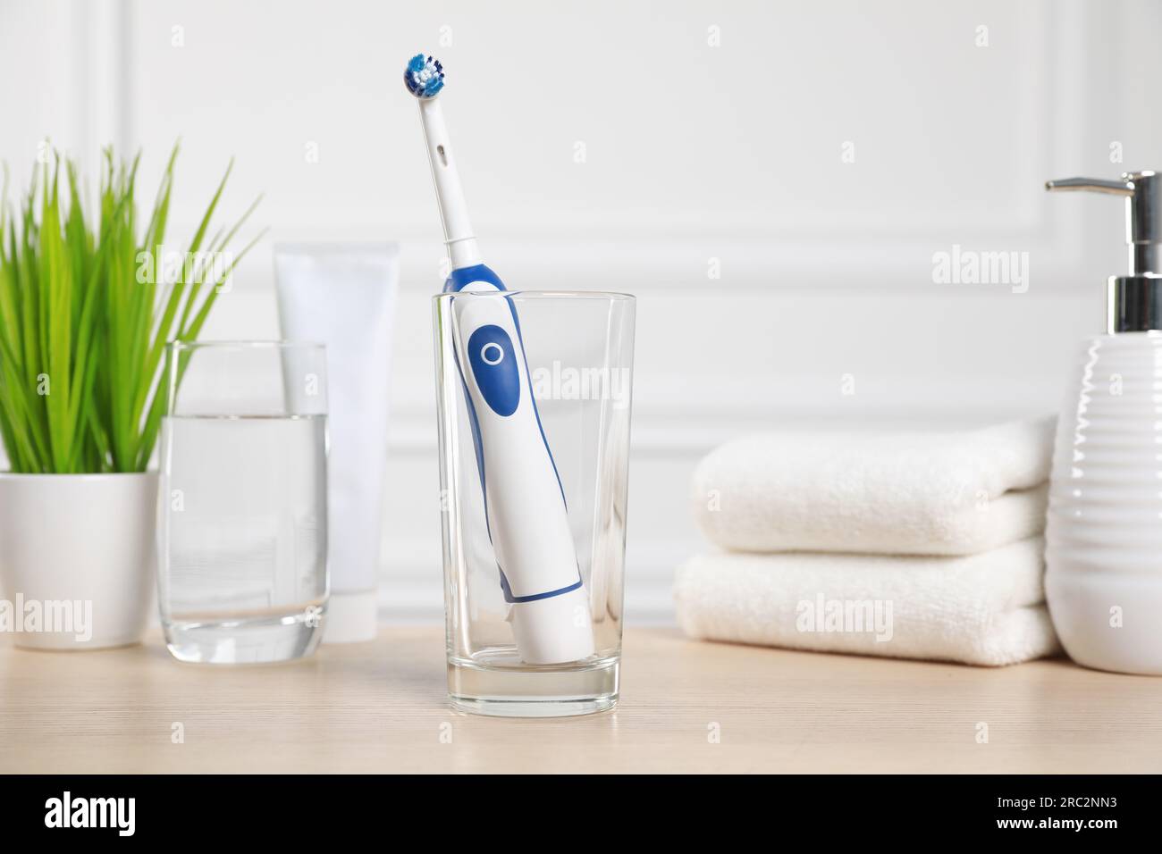 Electric toothbrush, glass of water and toiletries on wooden table ...