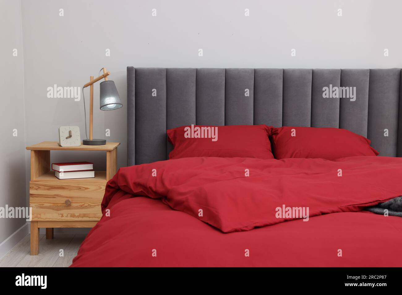 Comfortable bed, lamp, alarm clock and books on wooden bedside table in