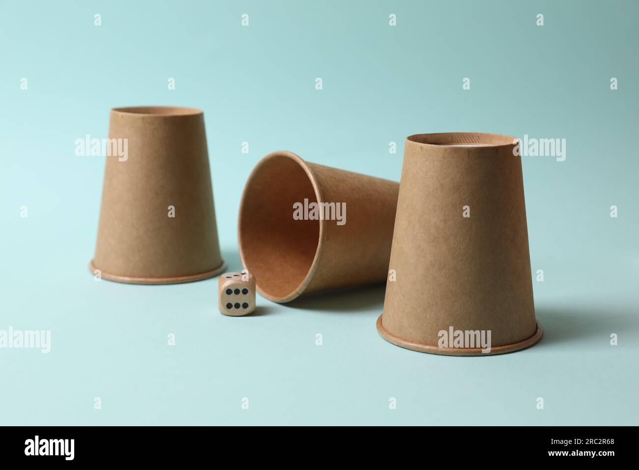 Three paper cups and dice on light blue background. Thimblerig game ...