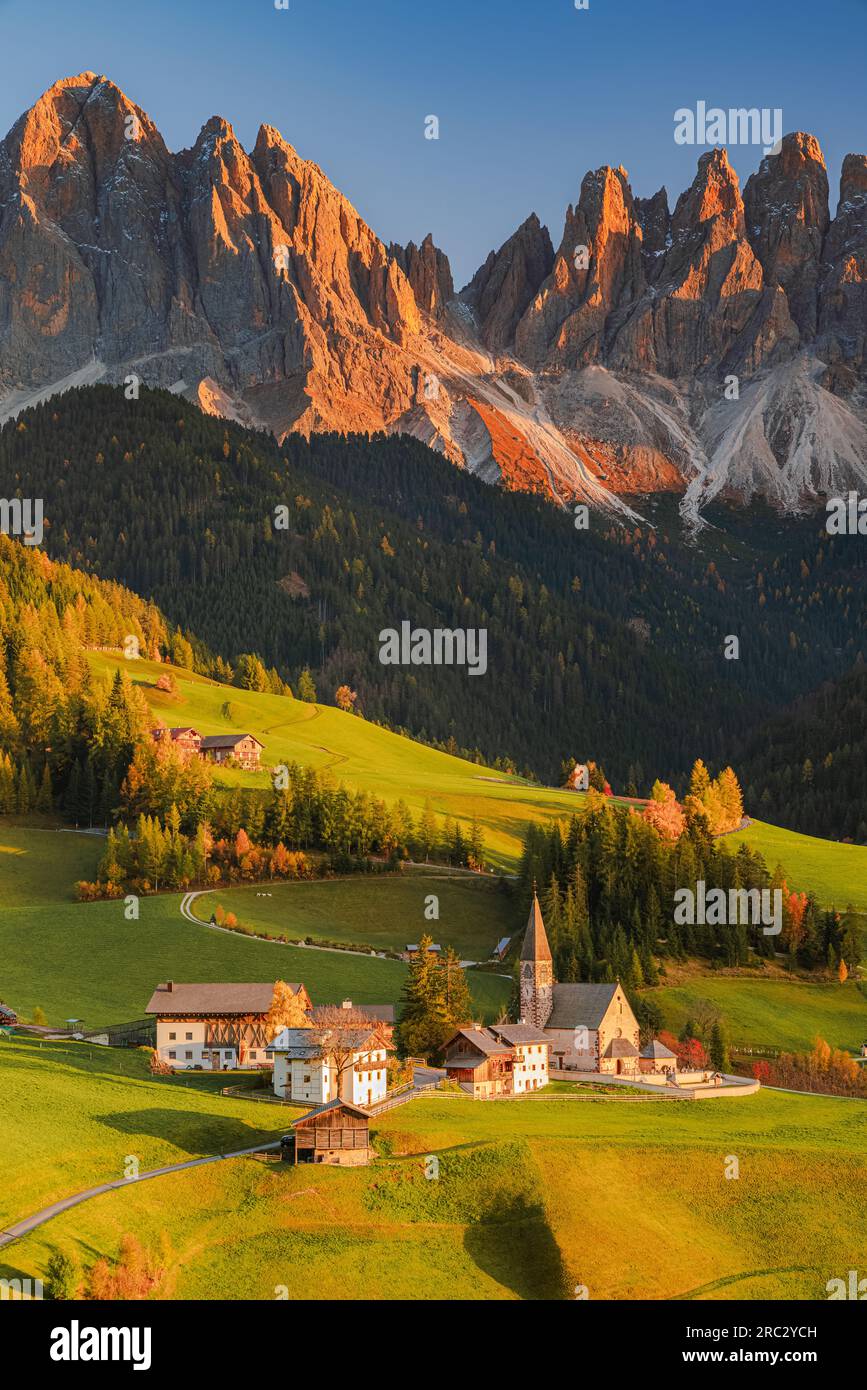 A vertical image from an autumn sunset at the famous church and village of Santa Maddalena in front of the Geisler / Odle Dolomites mountain peaks in Stock Photo