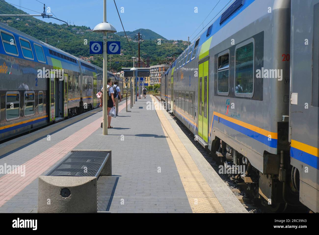 June 2023 La Spezia, Italy: Railway station, passengers with suitcases and fast trains across the mountains landscape Stock Photo