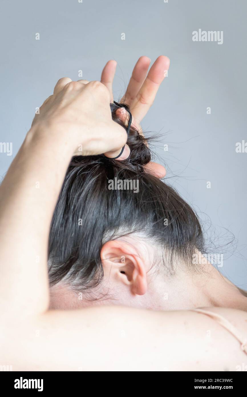 Detail of a young caucasian woman making a bun with her hair. Close-up view of a hair routine. Carefree and practical lifestyle concept. Stock Photo